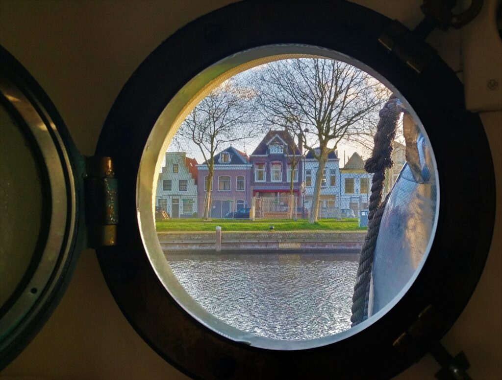 Vista di una tipica casa olandese attraverso l'oblò di una barca nei canali di Amsterdam, Paesi Bassi.