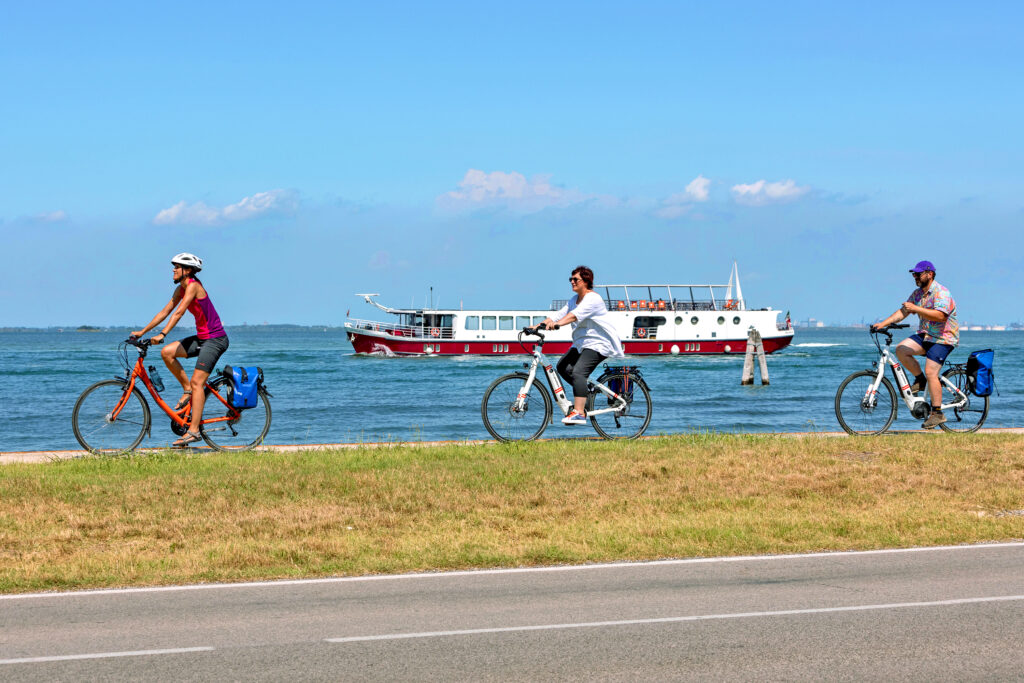 Ciclisti in viaggio con Girolibero lungo le piste ciclabili da Mantova a Venezia, con vista sul mare e cielo azzurro